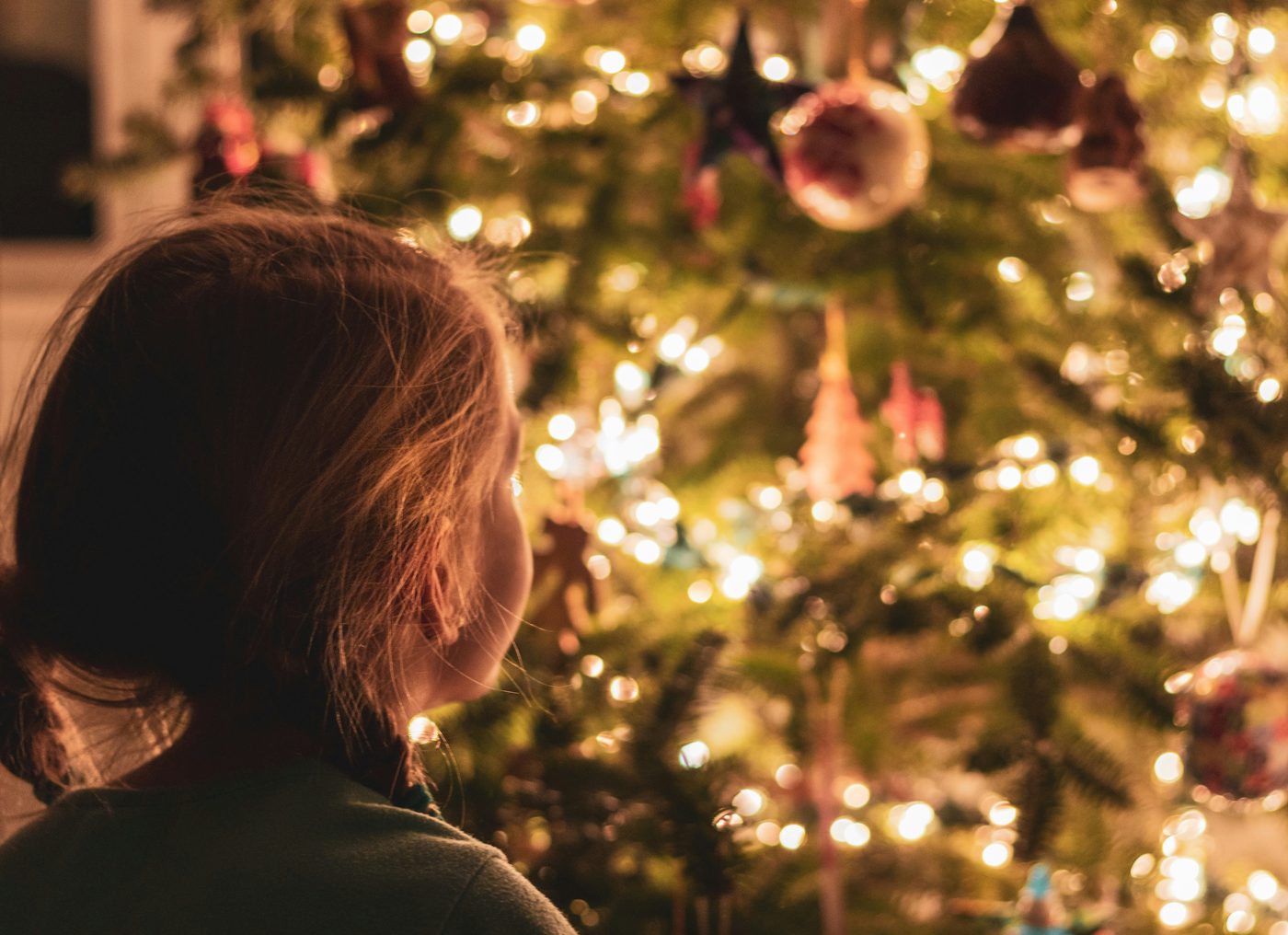 A young girl gazing up at a lit Christmas tree